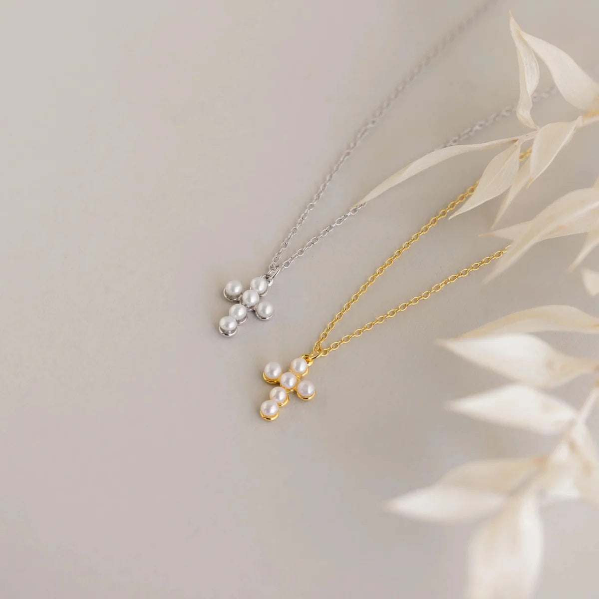 Two pearl necklaces, one gold and one silver, on a light background with leaves.
