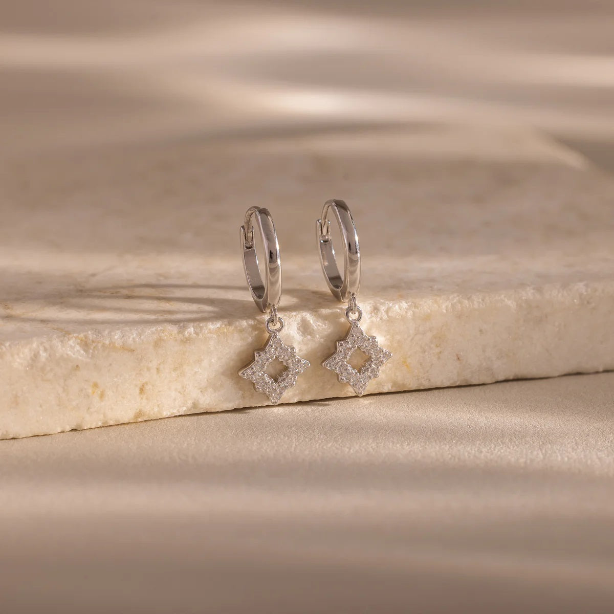 Silver hoop earrings with diamond-like stones on a beige stone surface