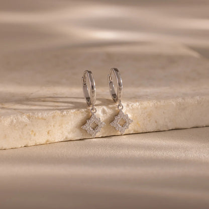 Silver hoop earrings with diamond-like stones on a beige stone surface