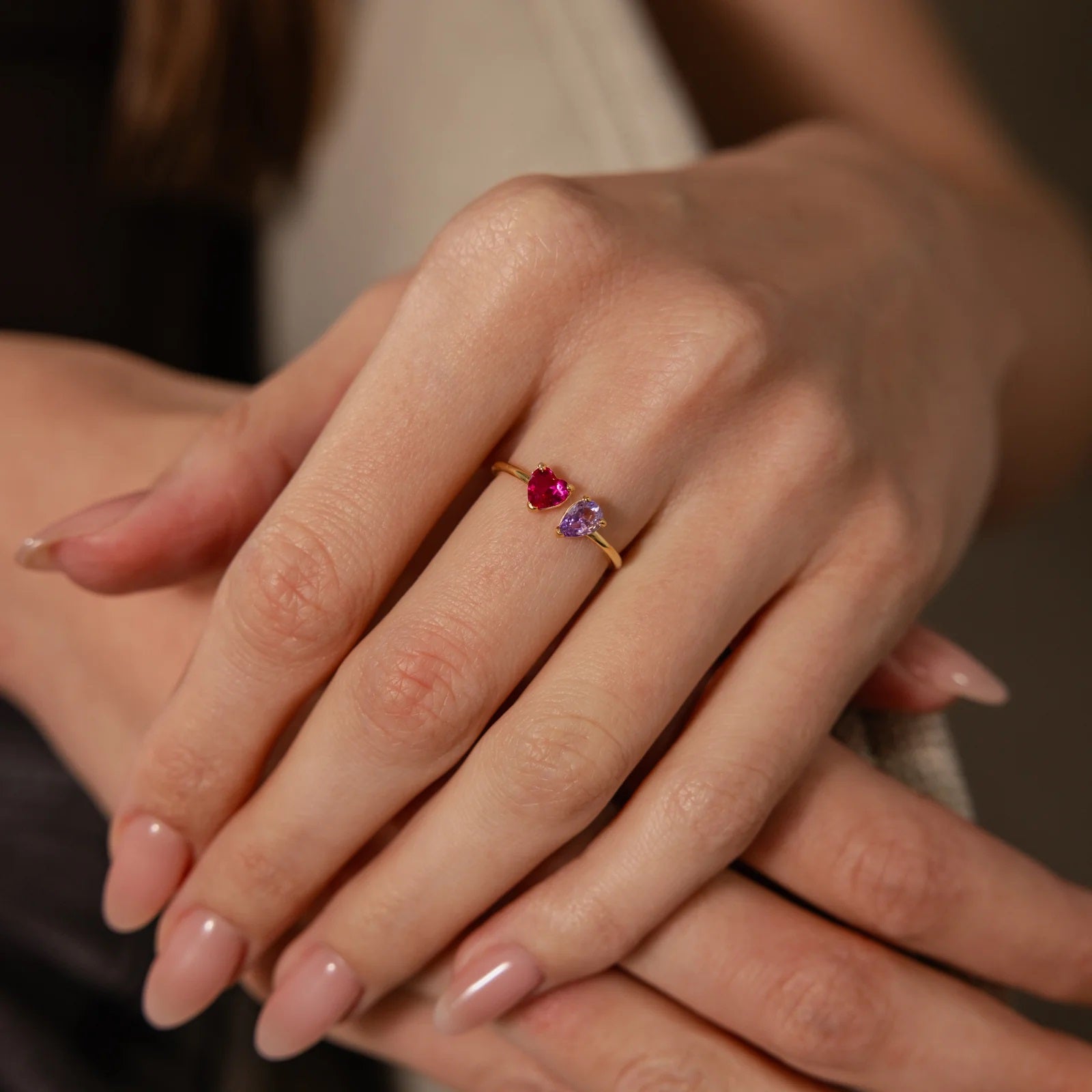 Close-up of a hand wearing a gold ring with a red gemstone and purple stone.