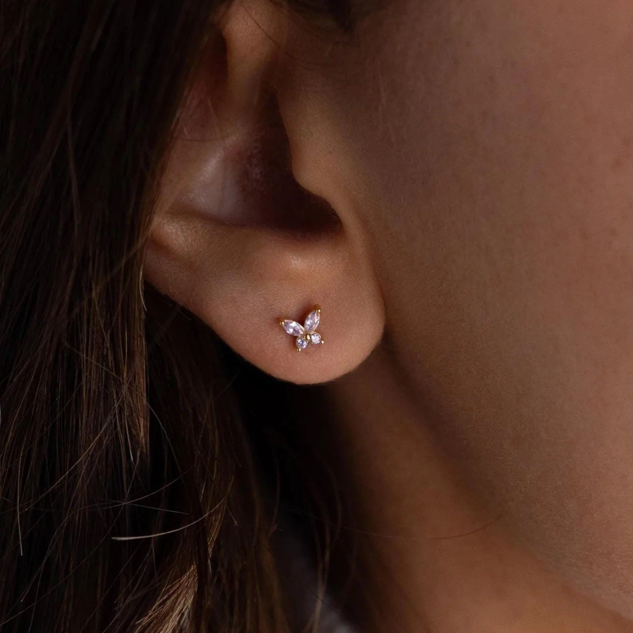 Close-up of an ear wearing a butterfly-shaped earring with a blurred background