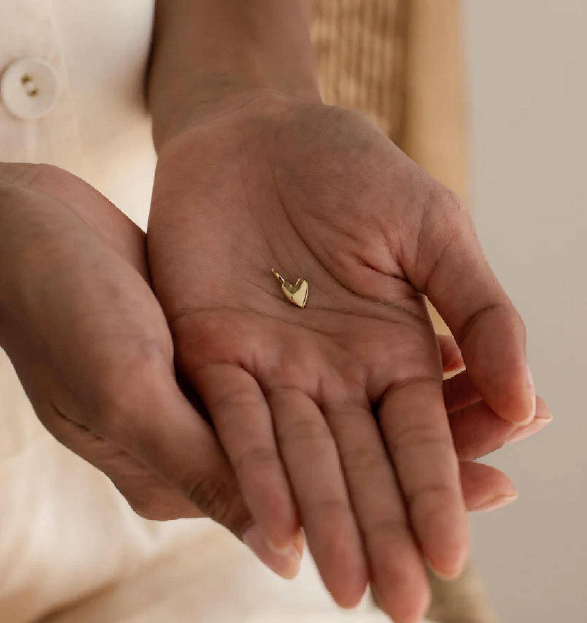 Gold heart-shaped earring held in a person's hand