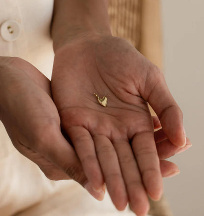 Gold heart-shaped earring held in a person's hand