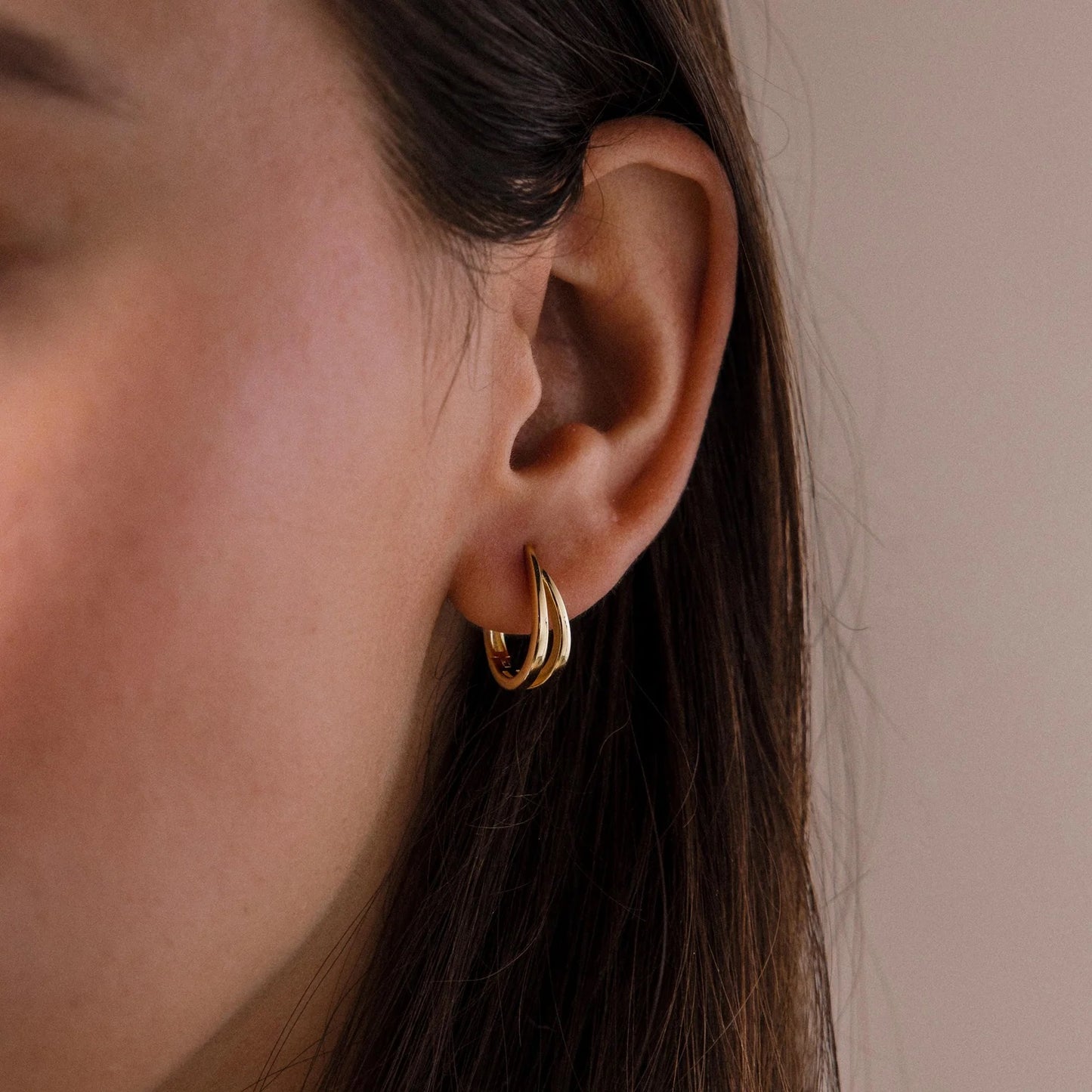 Close-up of a person wearing a gold hoop earring against a neutral background