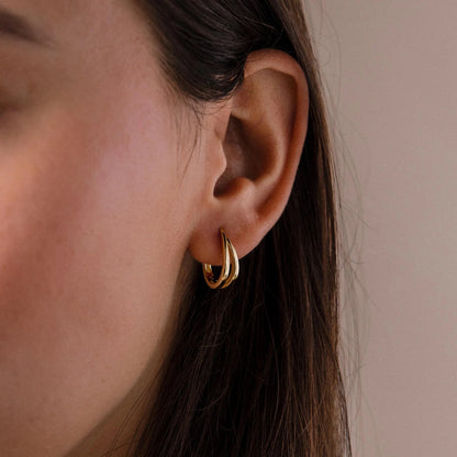 Close-up of a person wearing a gold hoop earring against a neutral background