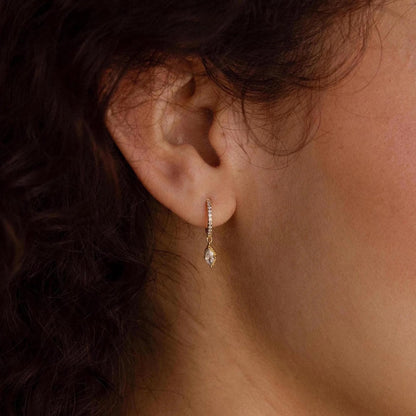 Close-up of an ear wearing a diamond earring with dark hair and skin in the background