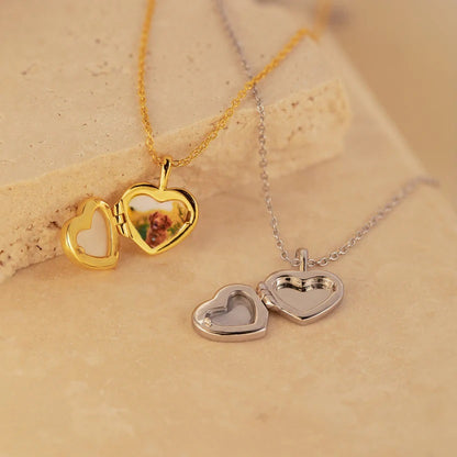 Two heart-shaped locket necklaces on a beige surface