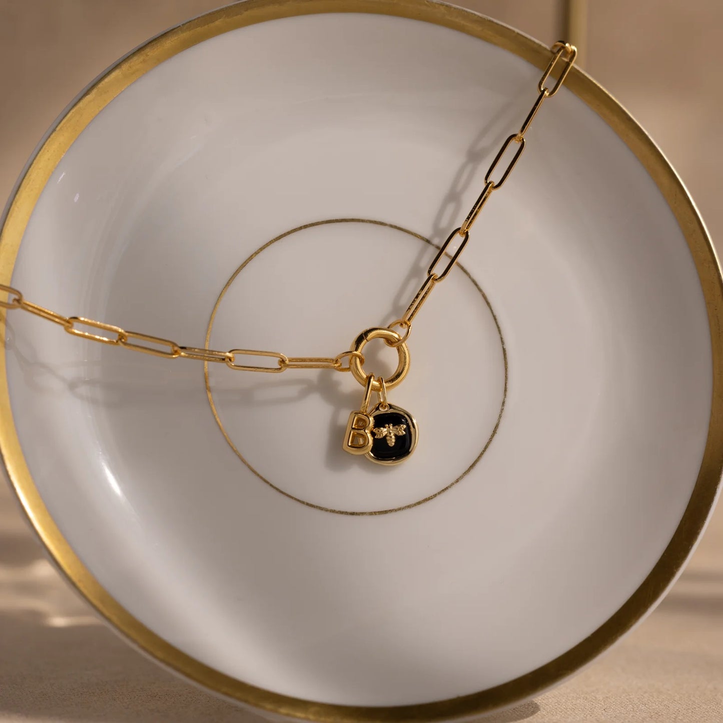 Gold chain necklace with a black lock charm on a white plate with gold rim.