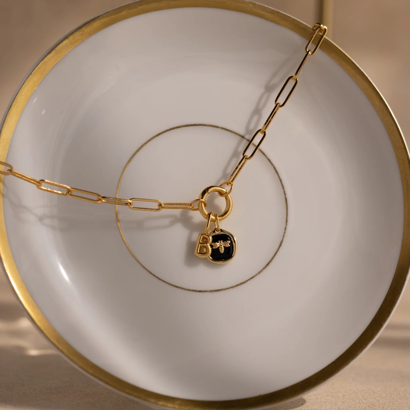 Gold chain necklace with a black lock charm on a white plate with gold rim.