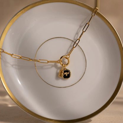 Gold chain necklace with a black lock charm on a white plate with gold rim.