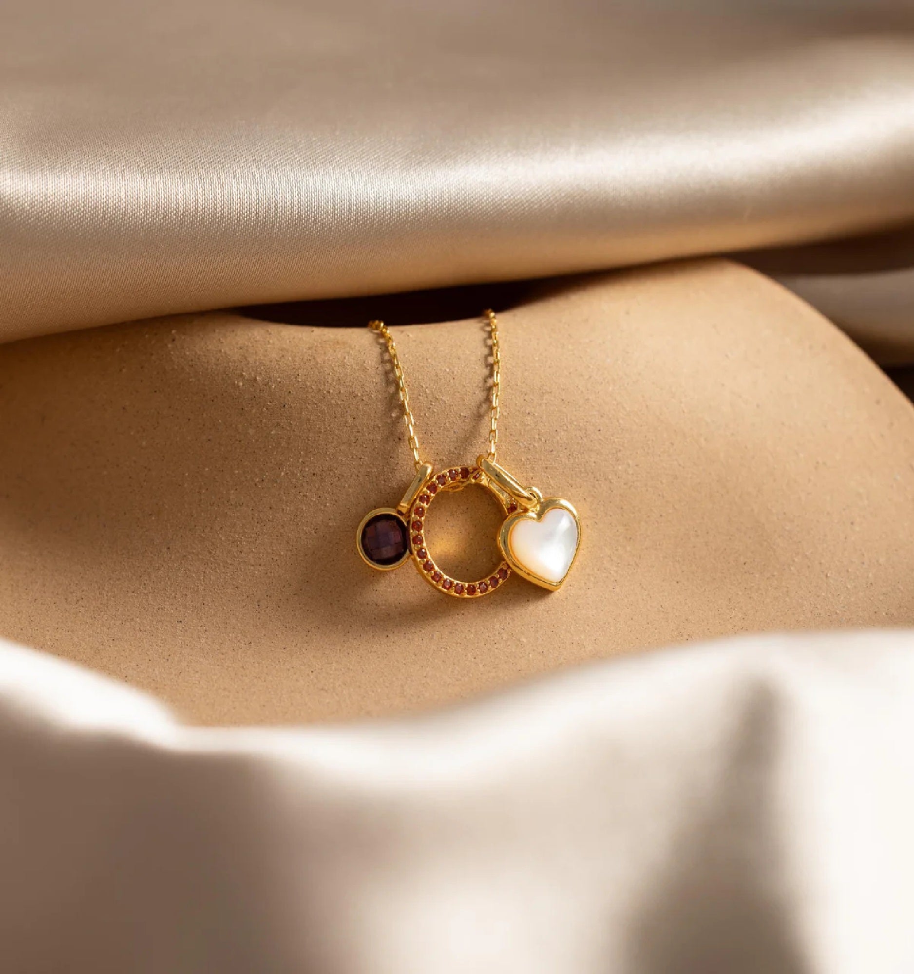 Gold necklace with heart and circle pendants on beige fabric