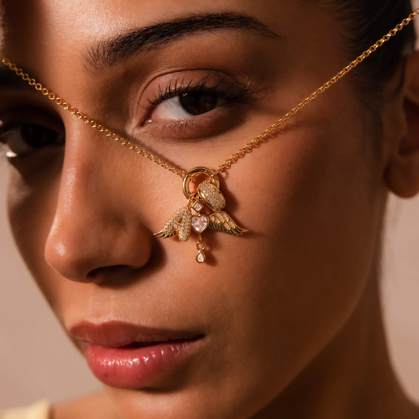 Close-up of a woman wearing a gold nose chain with angel wing and heart pendant.
