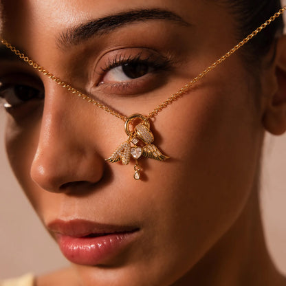 Close-up of a woman wearing a gold nose chain with angel wing and heart pendant.