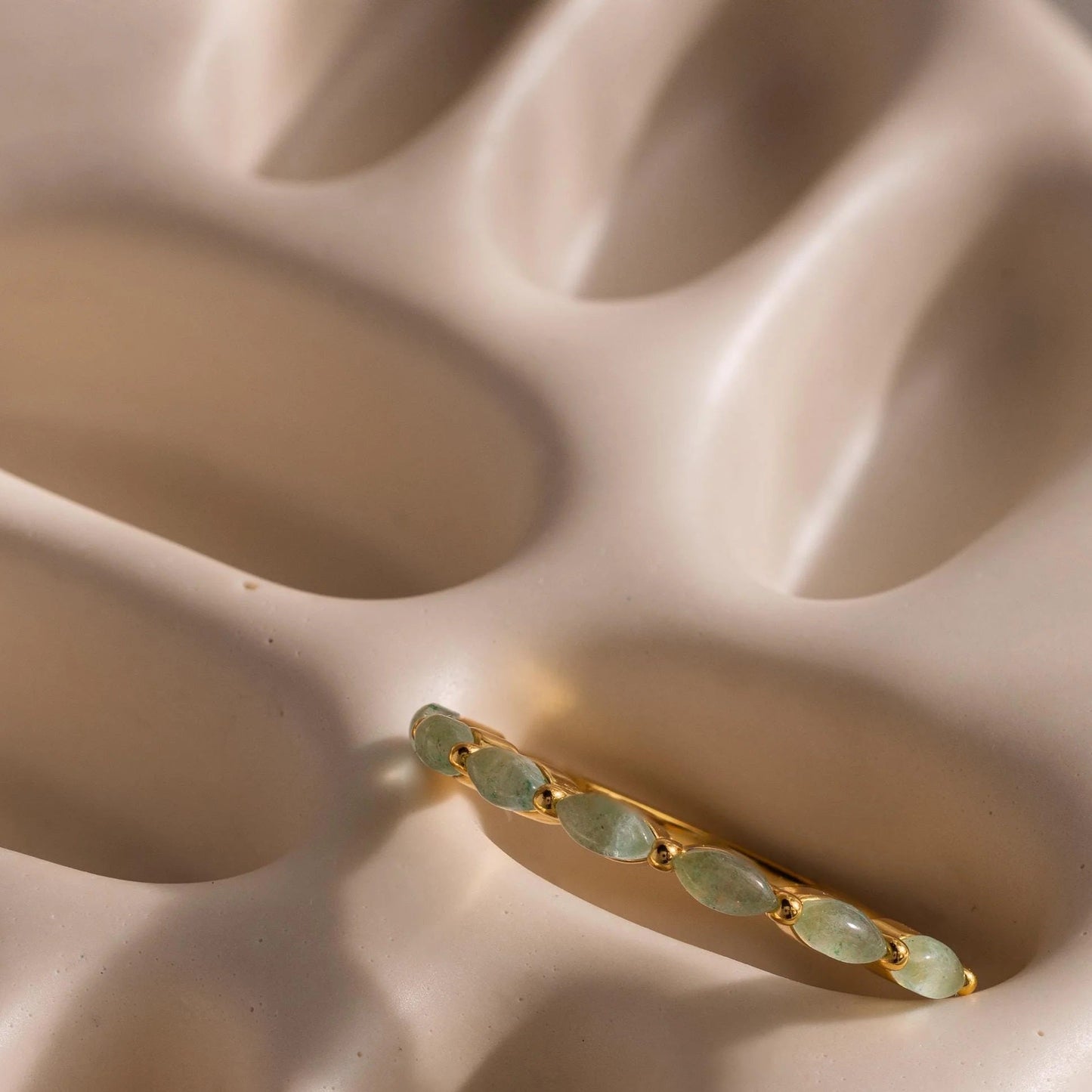 Gold earring with green gemstones on a beige surface