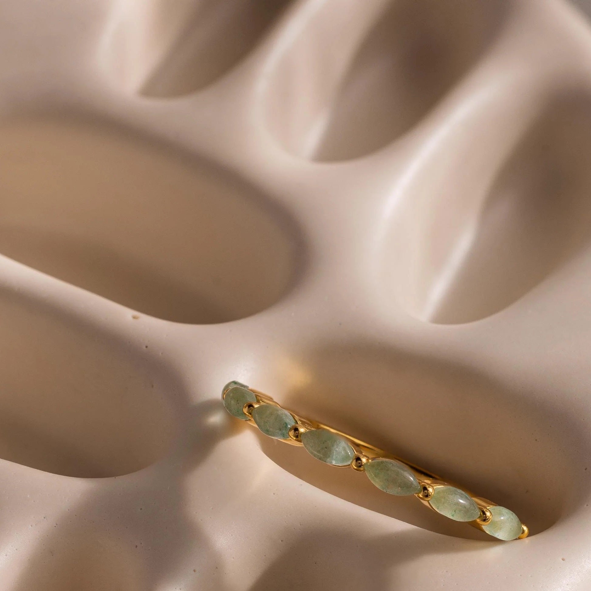 Gold earring with green gemstones on a beige surface