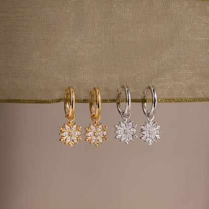 Two pairs of gold and silver hoop earrings with floral designs on a beige fabric background.