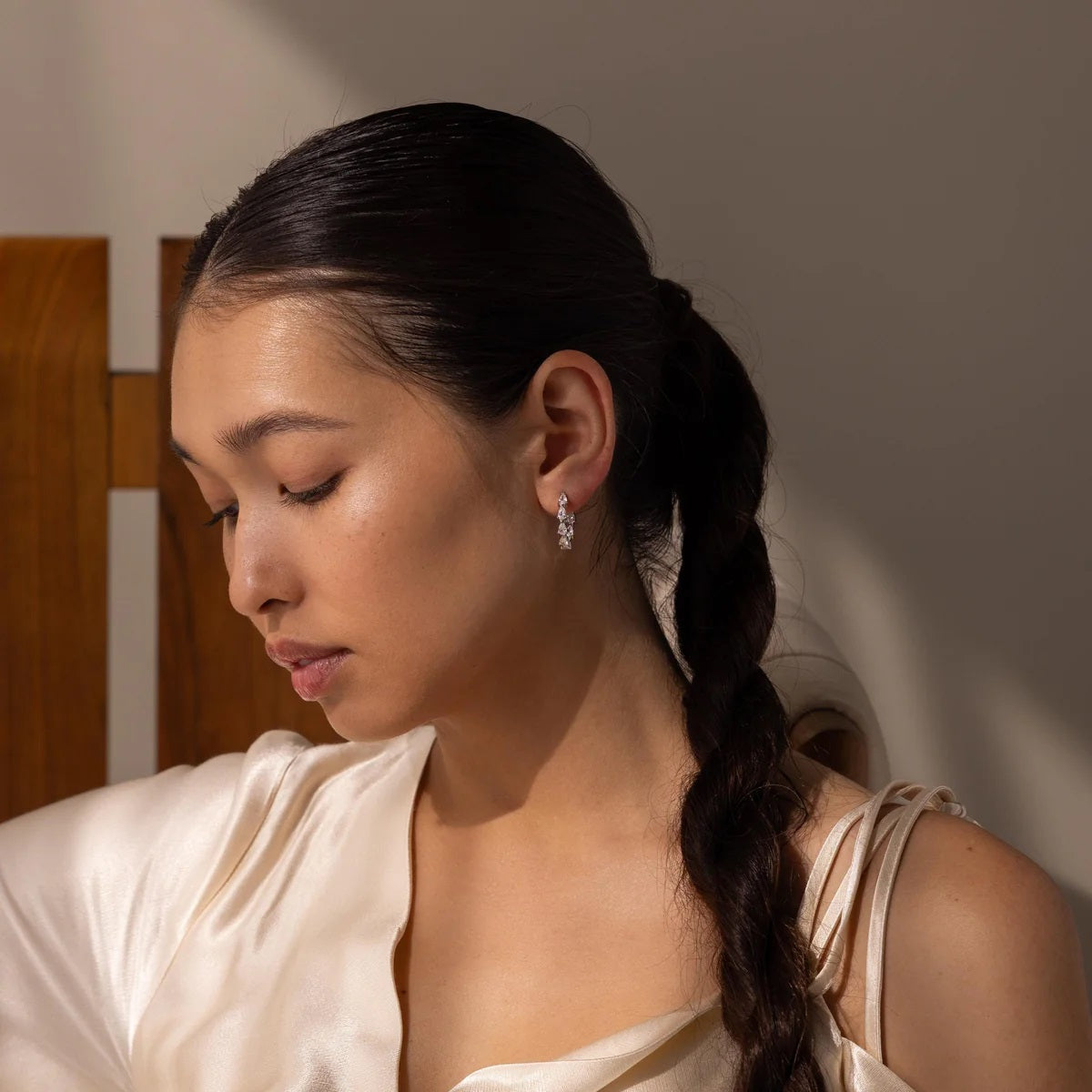 Woman with a braid wearing earrings against a neutral background