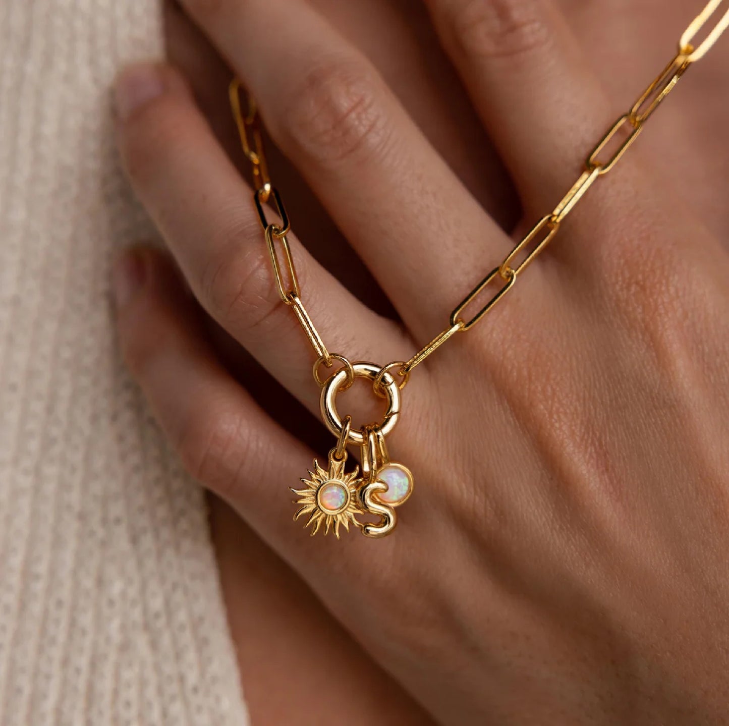 Gold chain bracelet with sun and moon charms on a hand against a neutral background