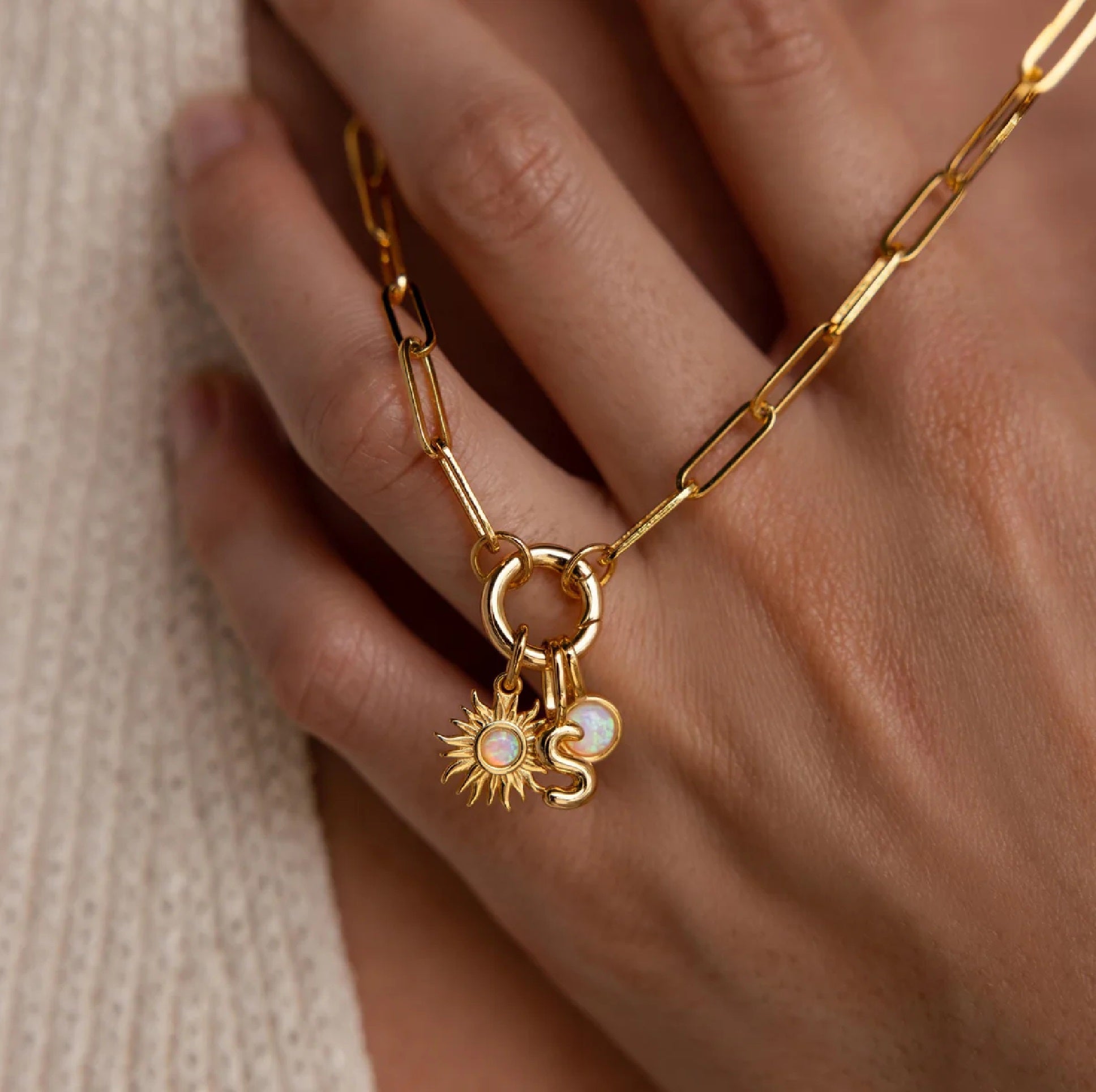 Gold chain bracelet with sun and moon charms on a hand against a neutral background