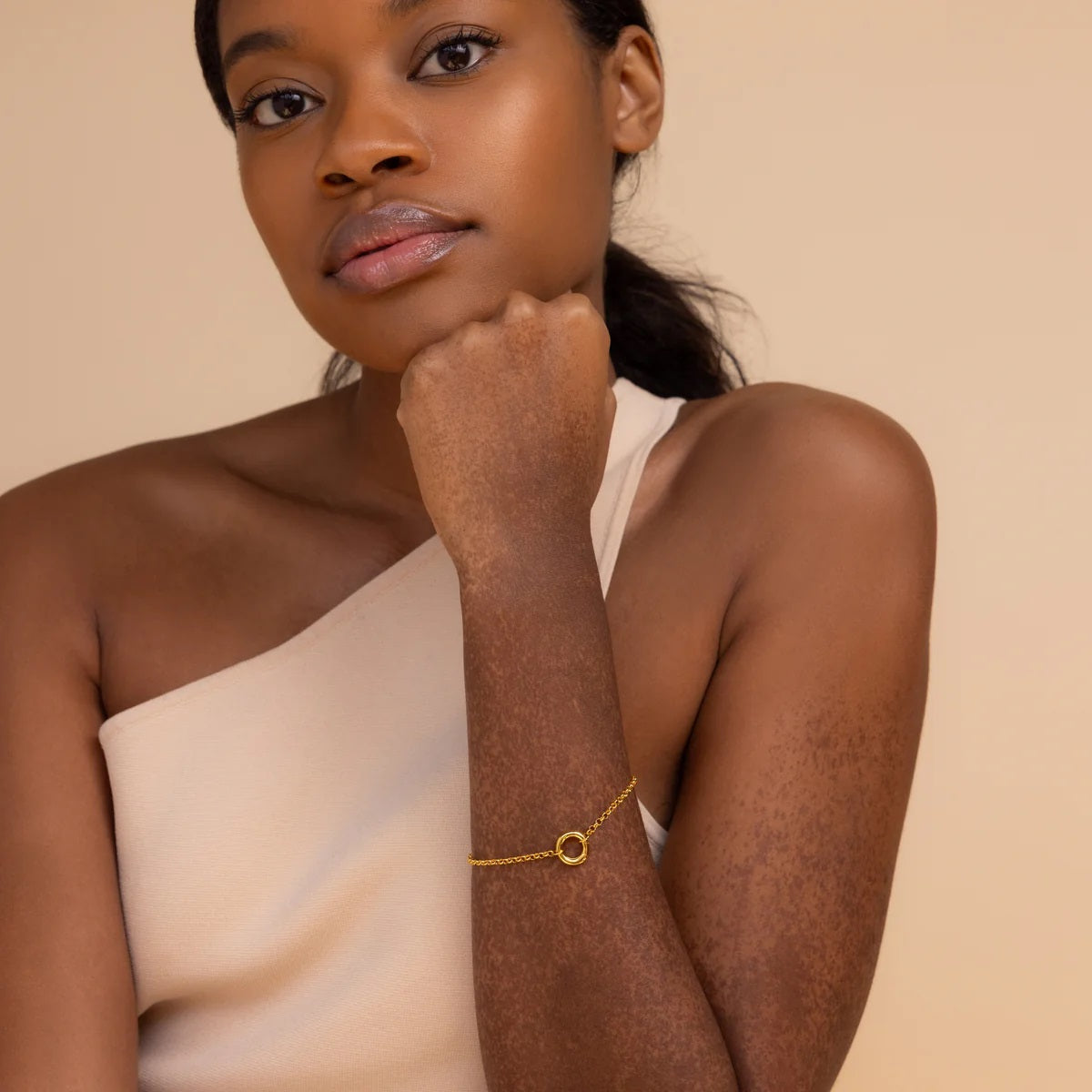 Woman wearing a gold bracelet on a beige background