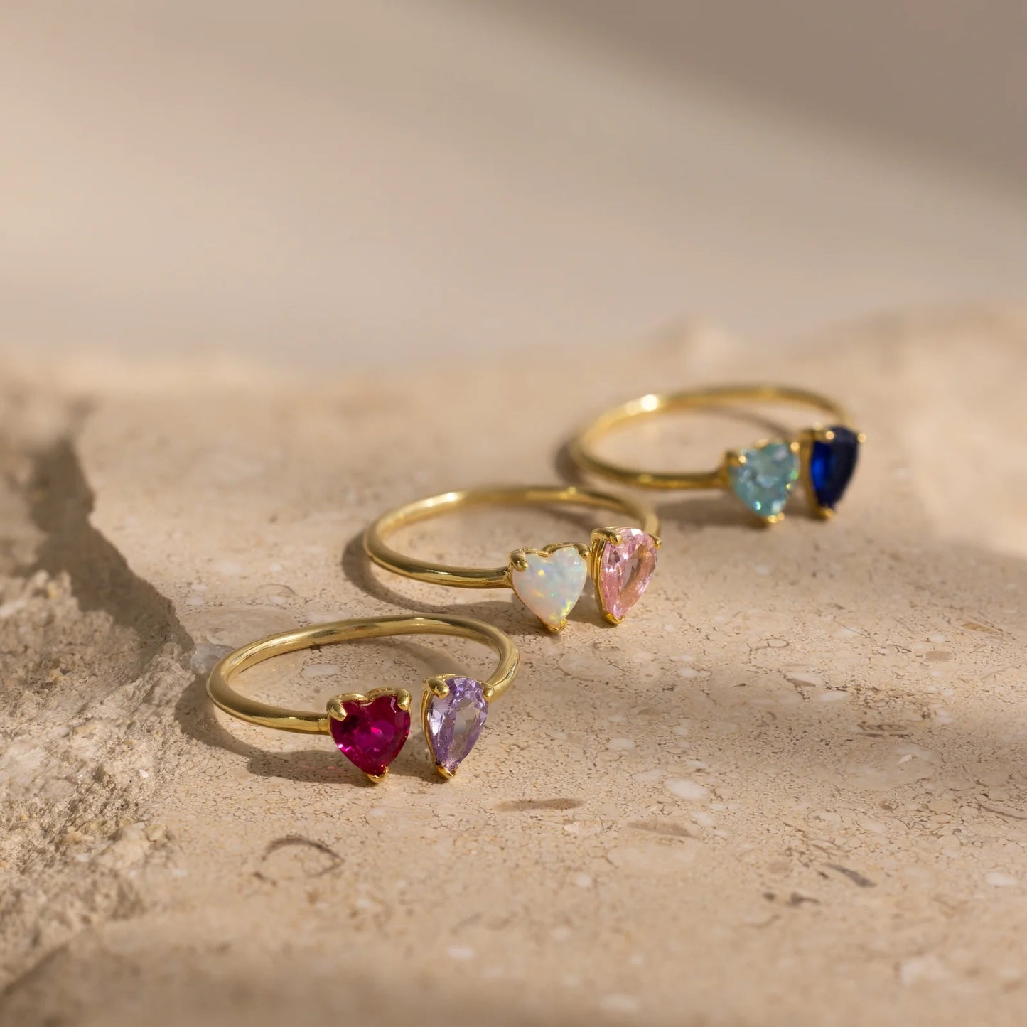 Set of gold rings with heart-shaped gemstones on a textured surface