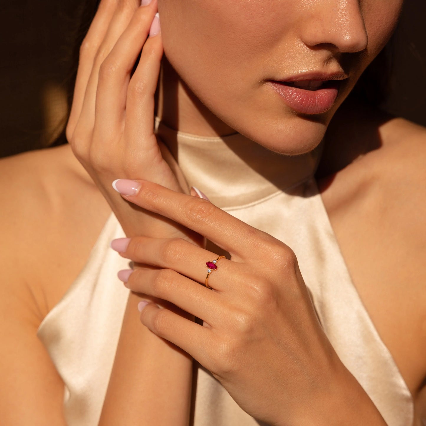 Close-up of a woman wearing a ring with a red gemstone, holding her hand near her face.