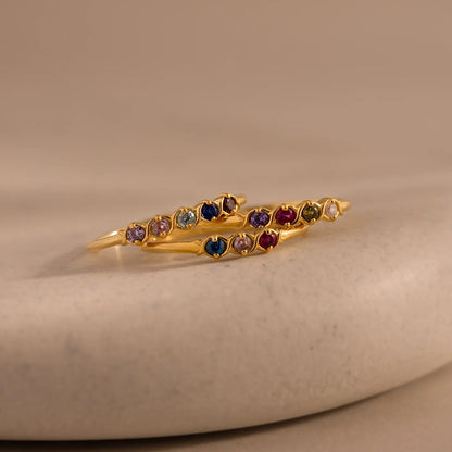 Gold bracelet with multicolored gemstones on a beige stone surface