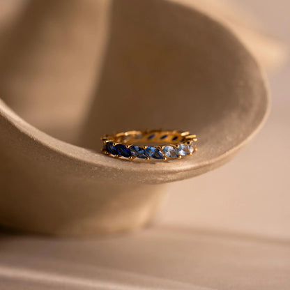 Gold ring with blue gemstones on a beige ceramic dish