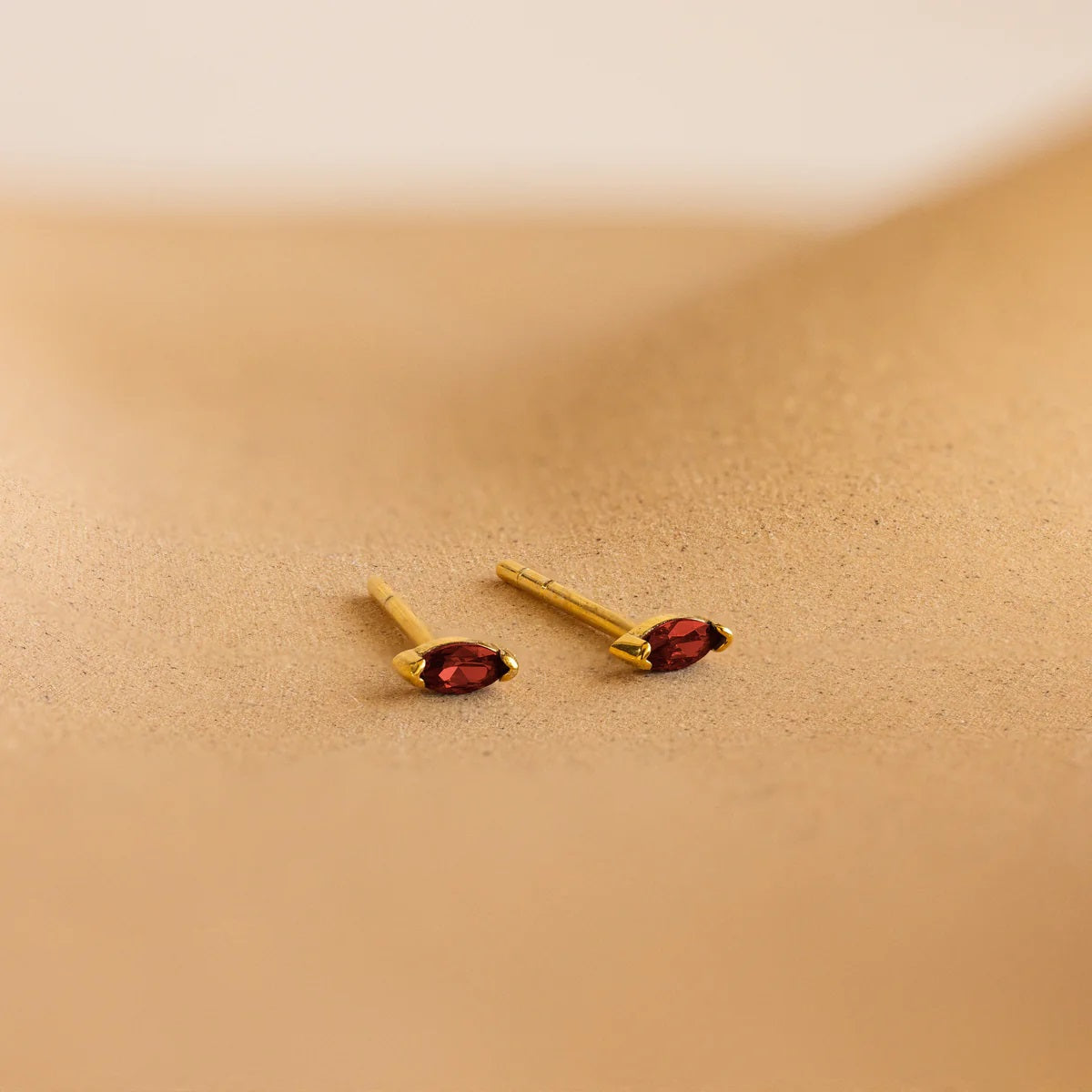 Gold earrings with red gemstones on a beige background