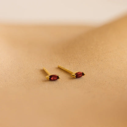 Gold earrings with red gemstones on a beige background
