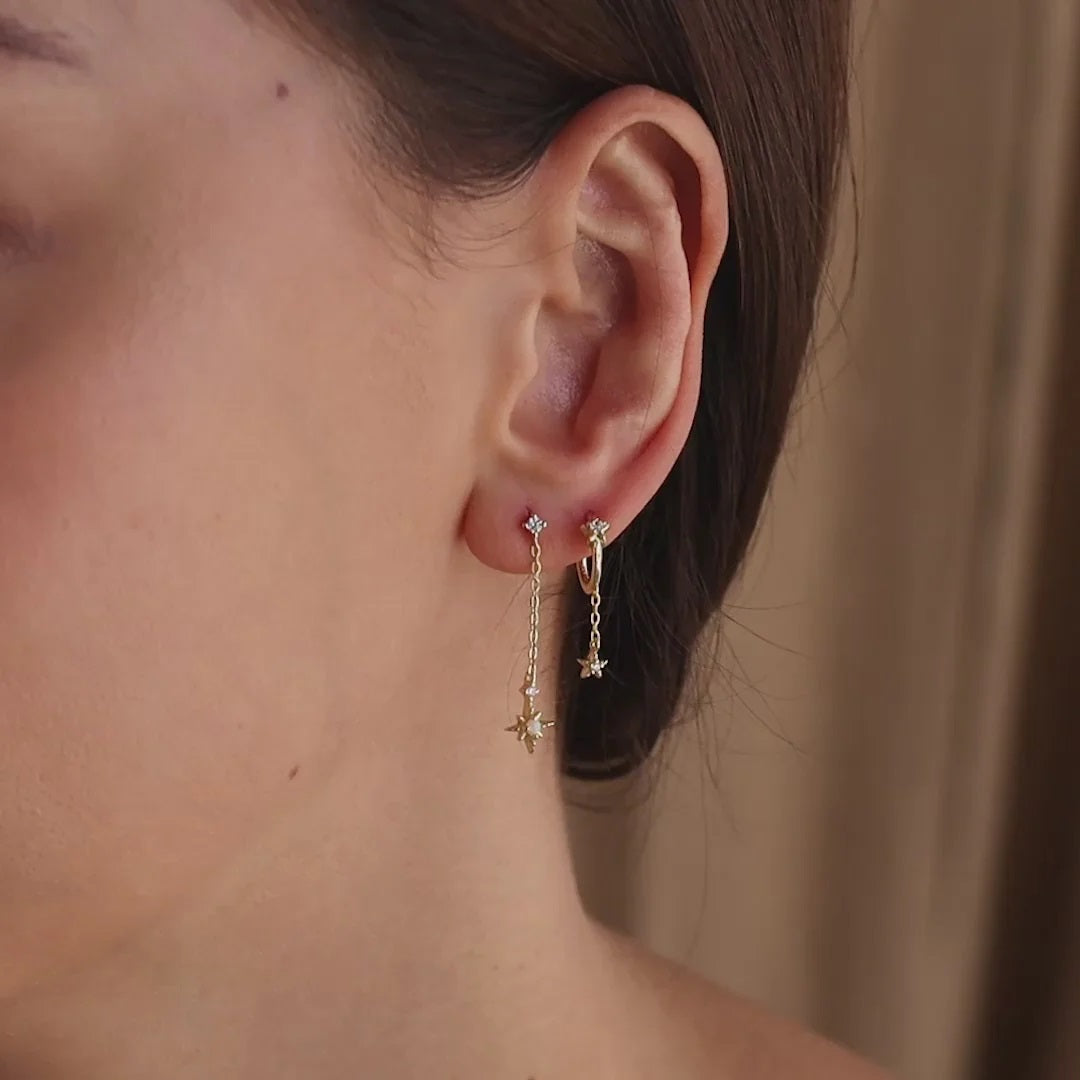 Close-up of an ear wearing gold earrings with a neutral background