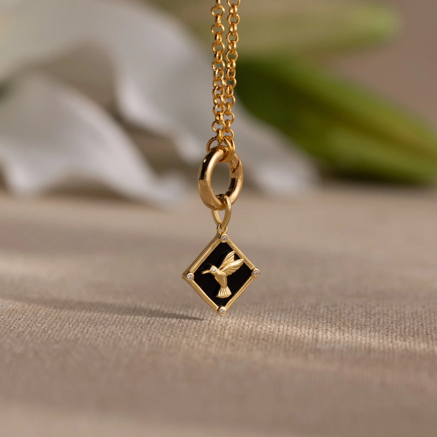 Gold necklace with a diamond-shaped pendant featuring a dove on a beige surface.