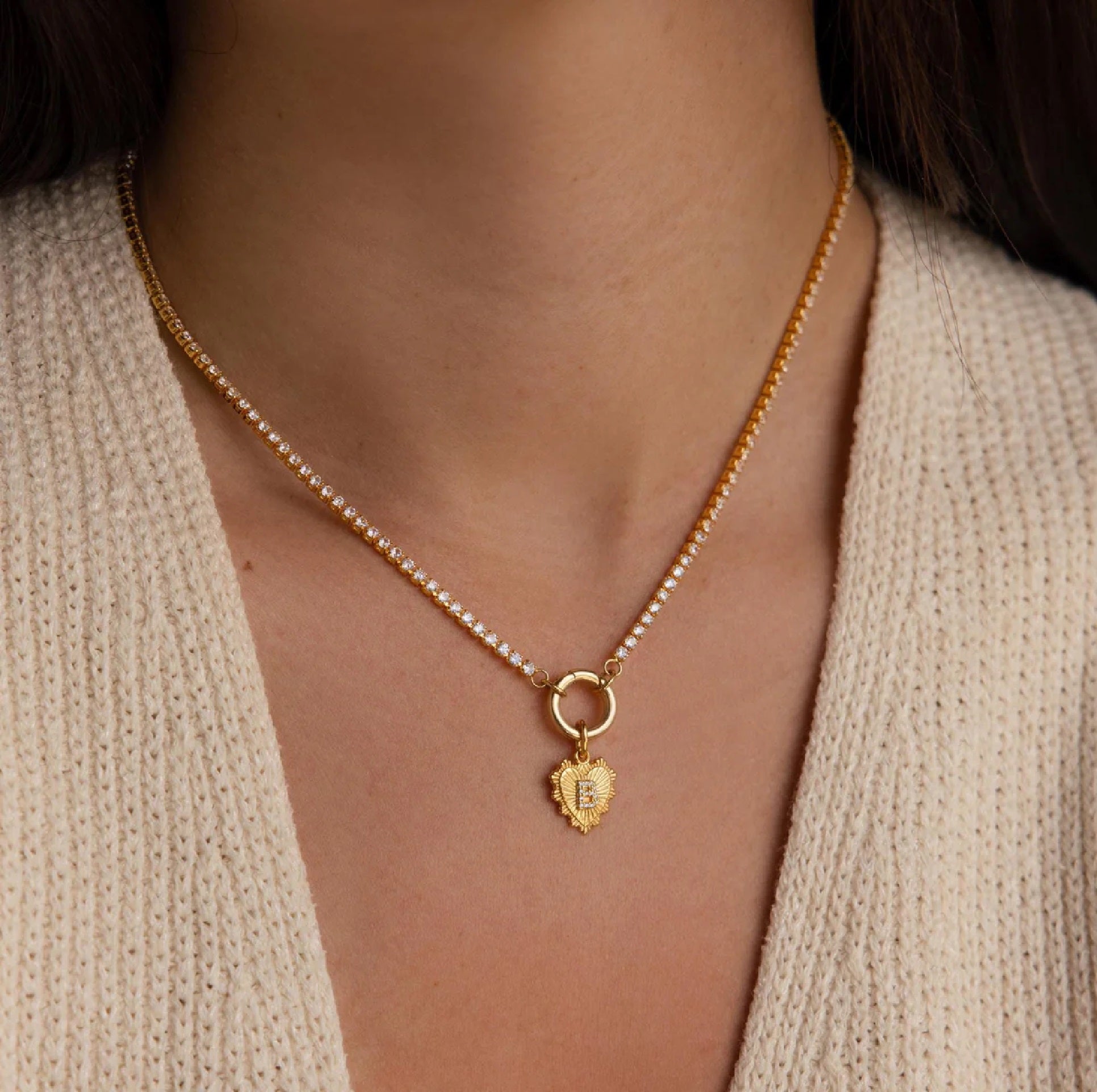 Gold necklace with a heart-shaped pendant worn by a person in a beige sweater.