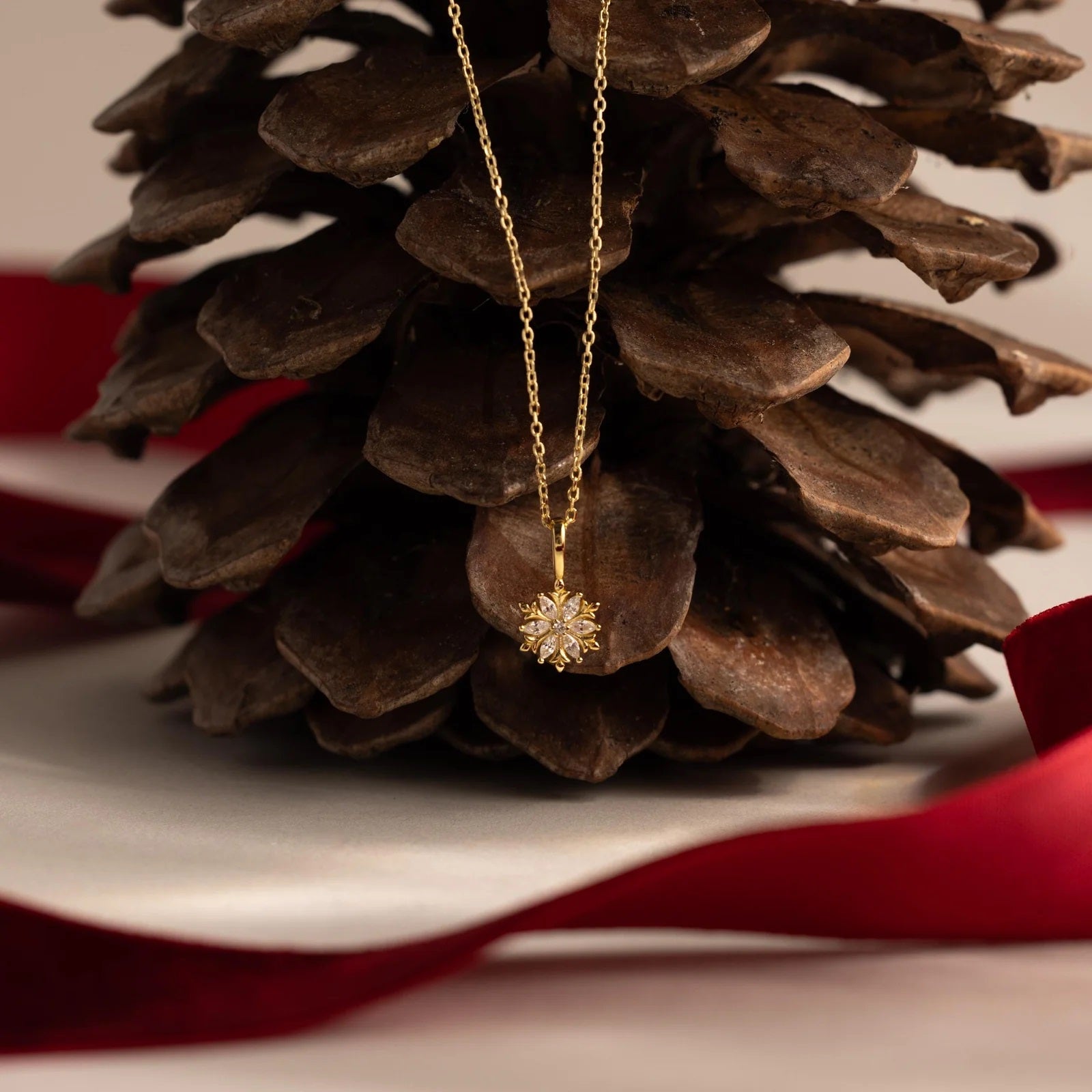 Gold necklace with a snowflake pendant on a pine cone with a red ribbon