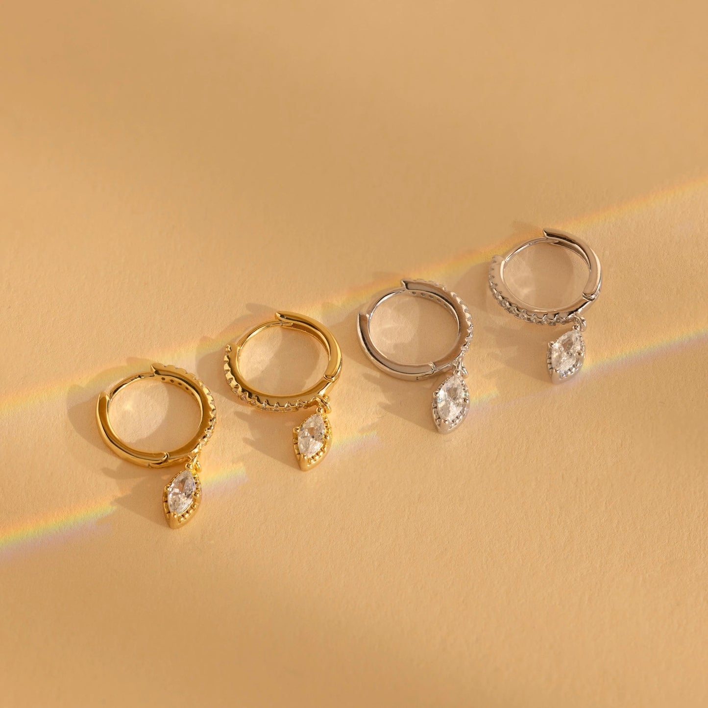 Set of gold and silver hoop earrings with teardrop-shaped gemstones on a beige background