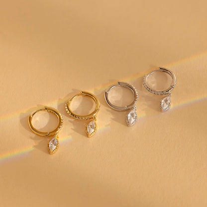 Set of gold and silver hoop earrings with teardrop-shaped gemstones on a beige background