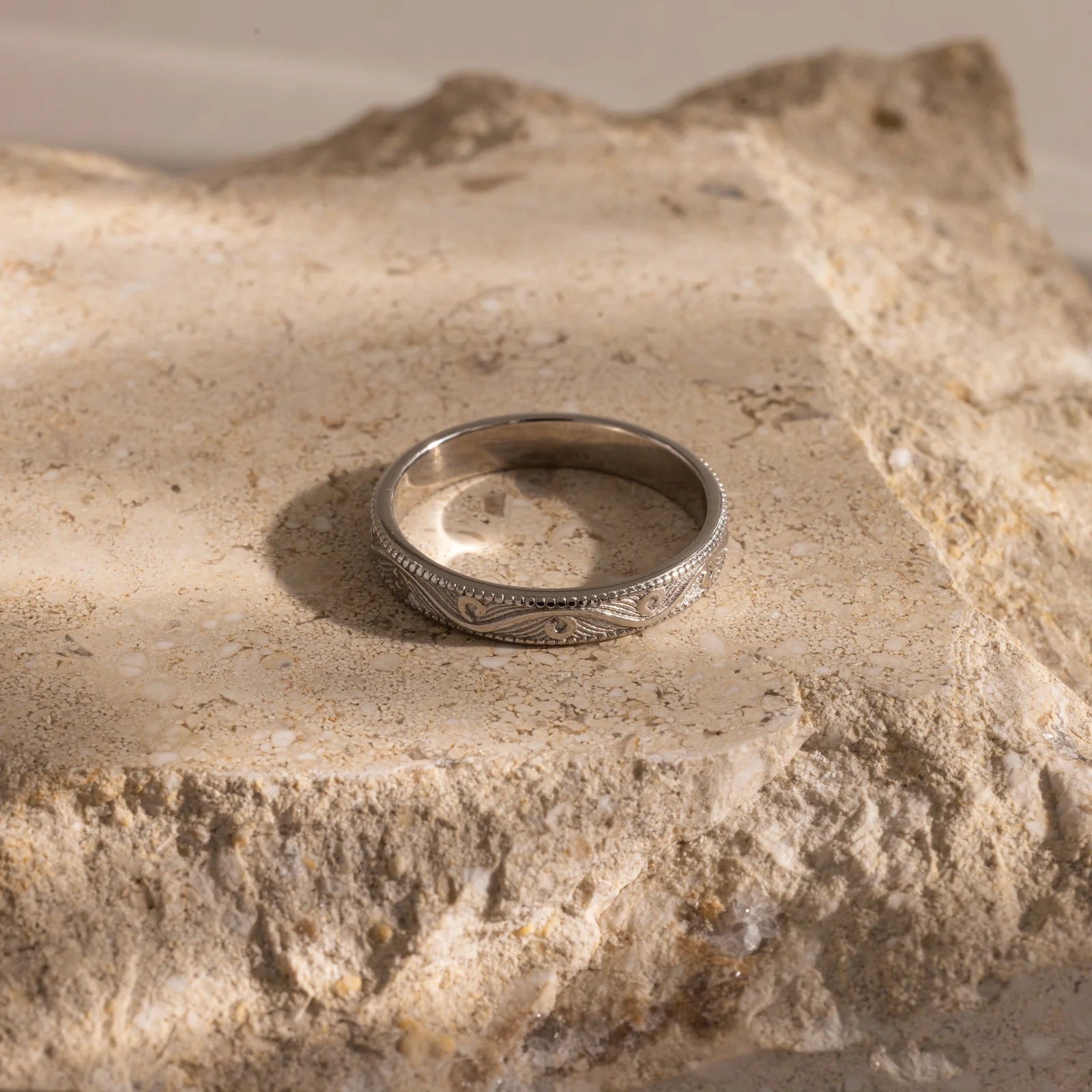 Silver ring with intricate design on a textured stone surface