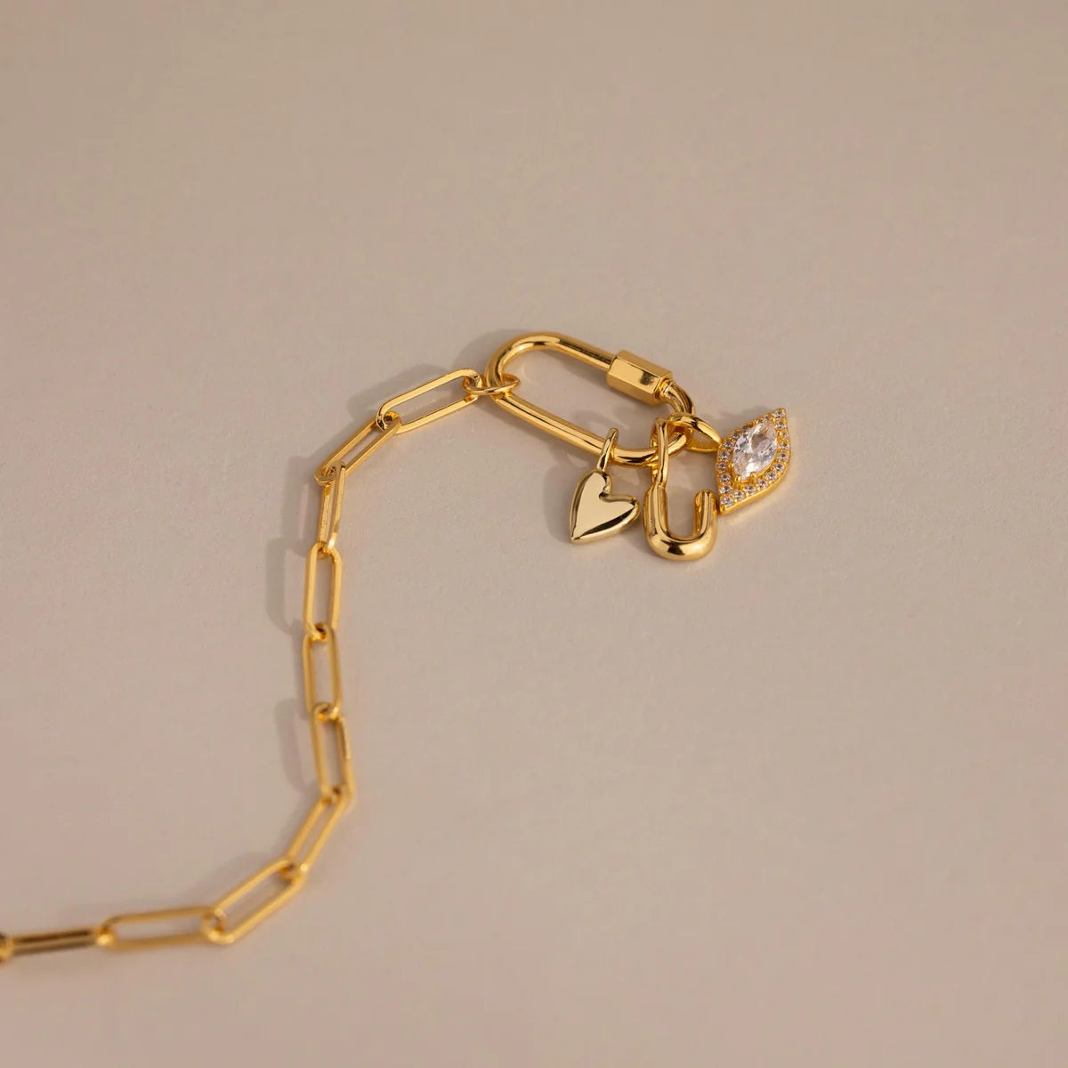 Gold bracelet with heart and diamond charm on a beige background