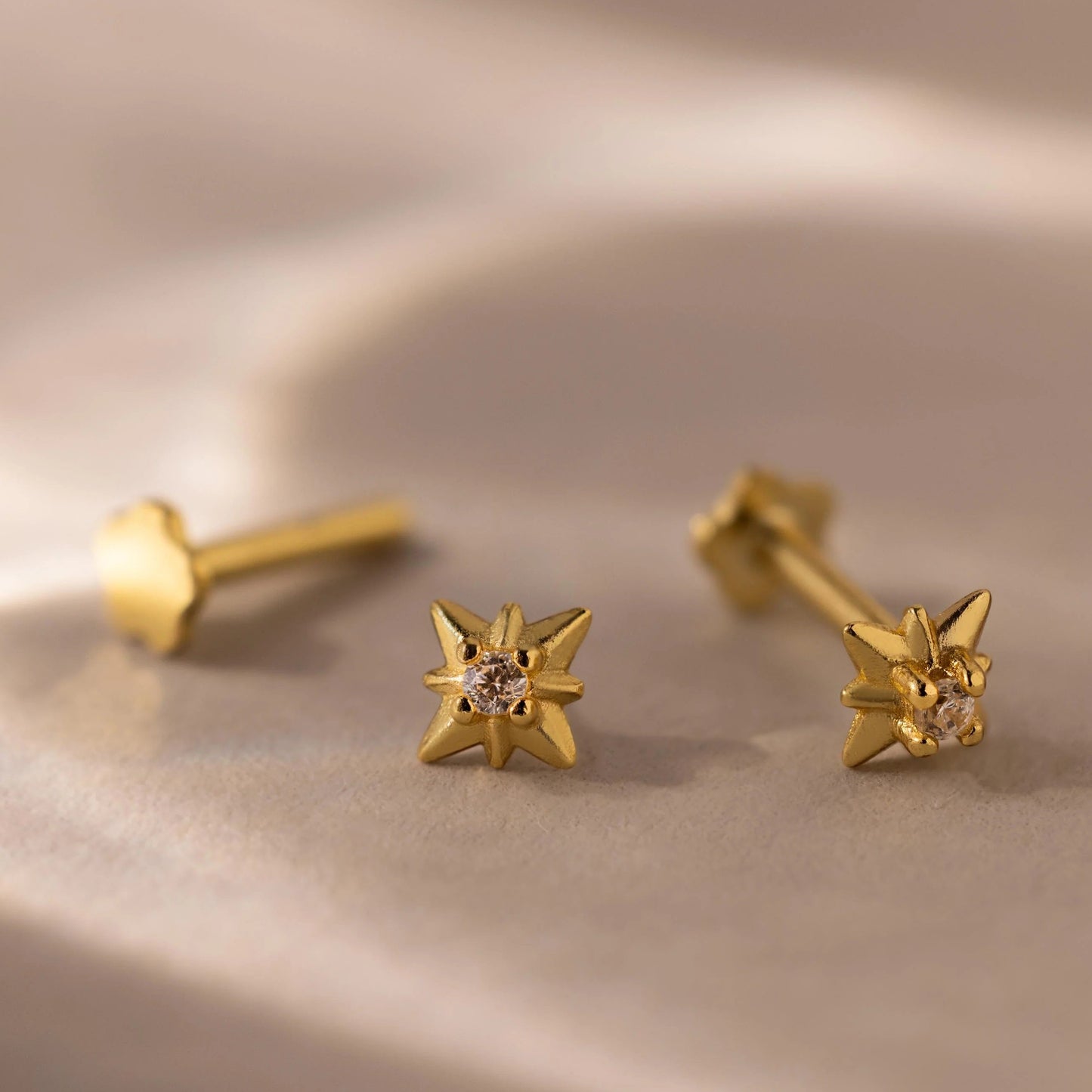 Gold star-shaped earrings with a central gemstone on a beige surface