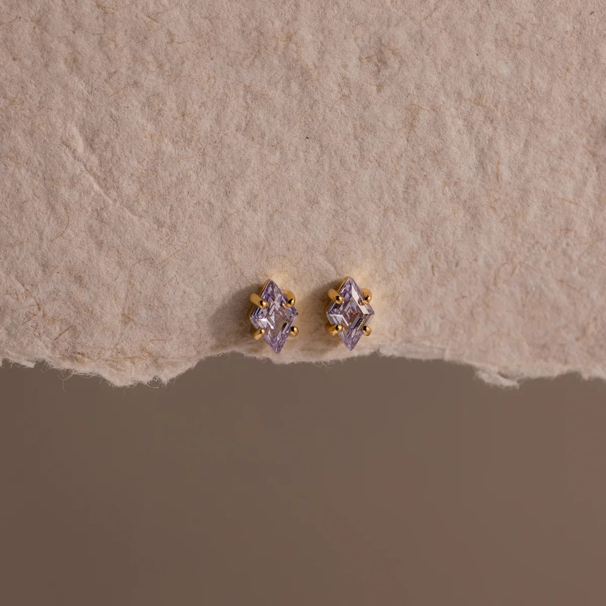 Pair of gold and purple stud earrings on a textured beige surface