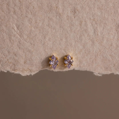 Pair of gold and purple stud earrings on a textured beige surface
