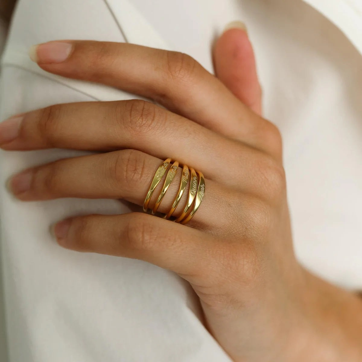 Hand wearing multiple gold rings on a white background