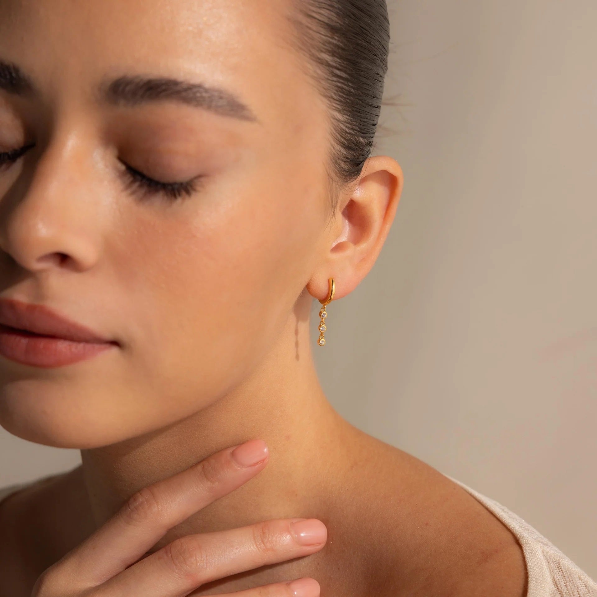 Close-up of a woman wearing gold earrings with a neutral background