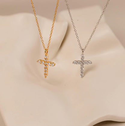 Two cross-shaped pendants on gold and silver chains against a beige background