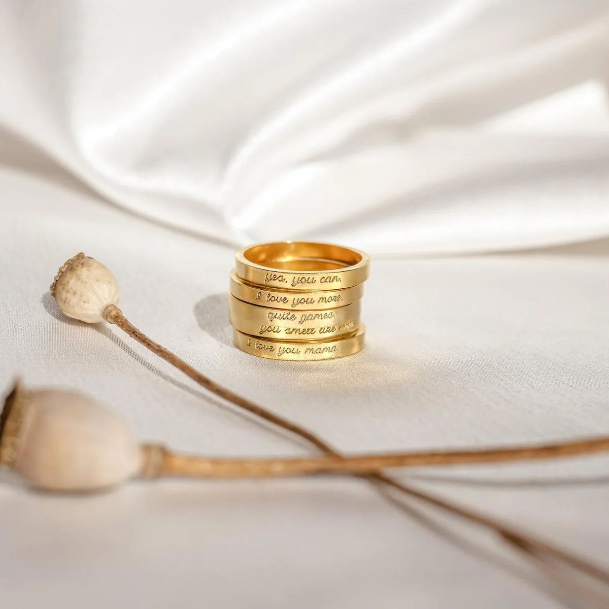 Stack of gold rings with engraved text on a white fabric background