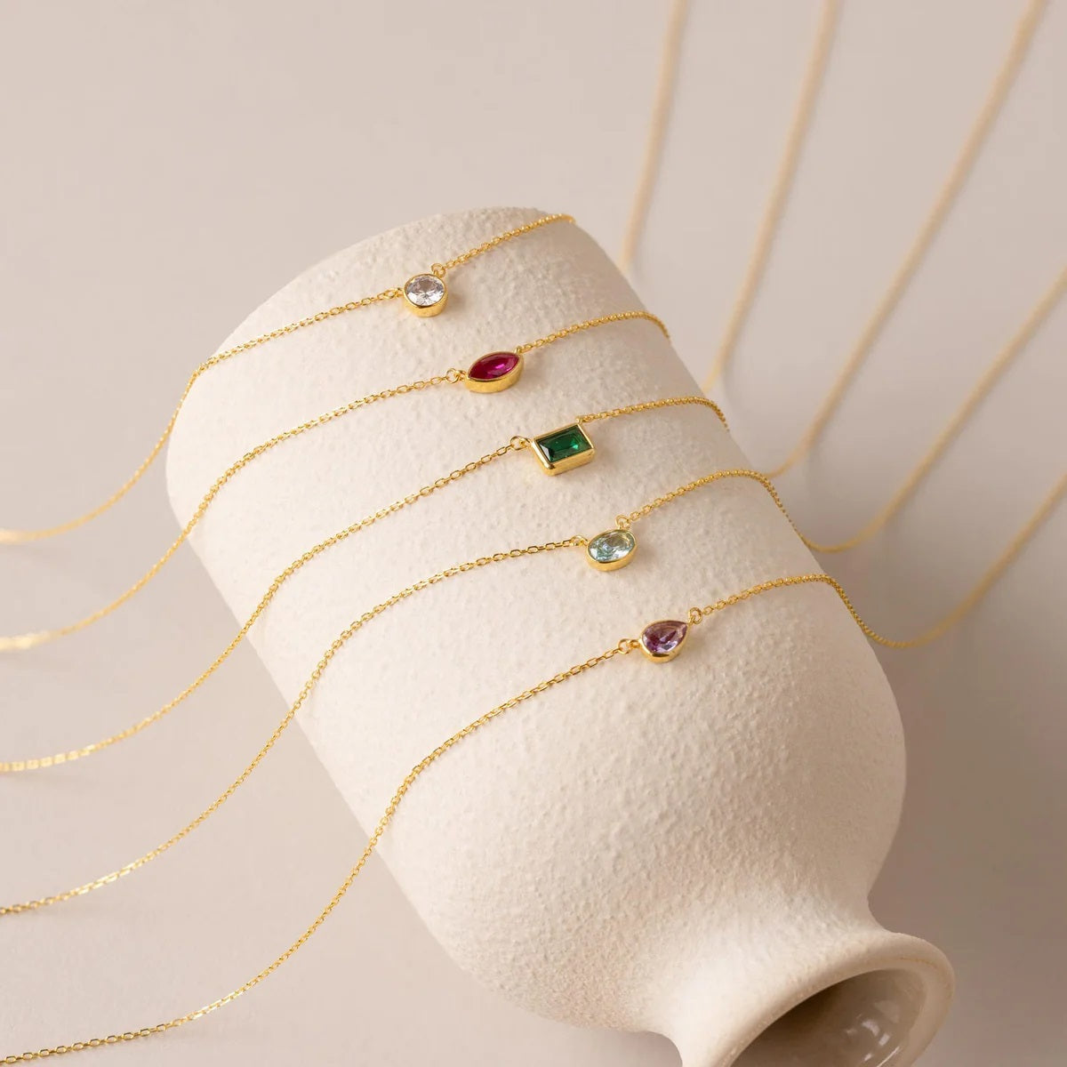 Gold necklaces with colorful gemstones on a white stand against a beige background