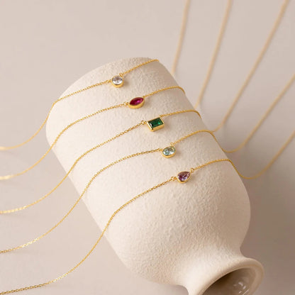 Gold necklaces with colorful gemstones on a white stand against a beige background