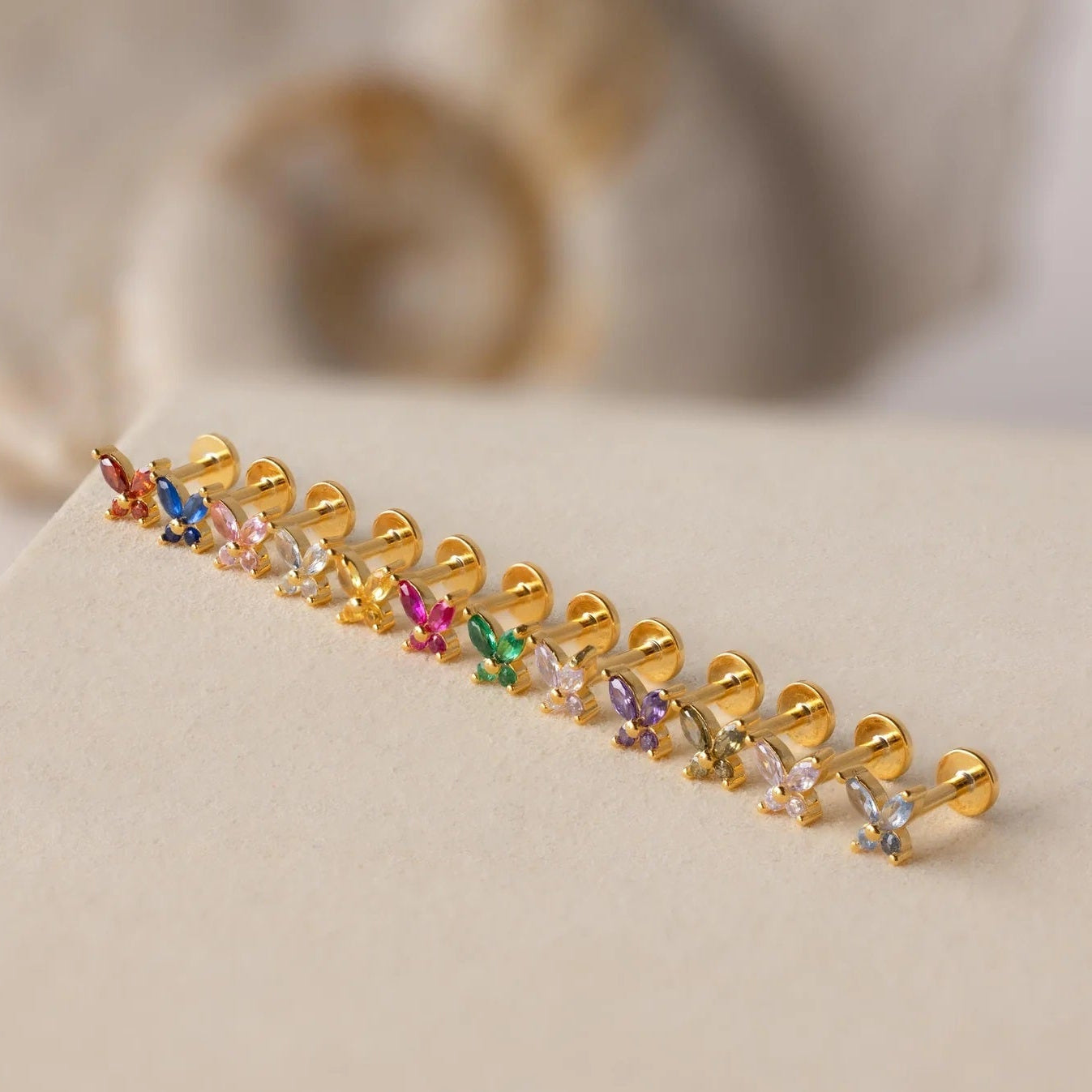 Gold earring with colorful gemstones on a beige surface