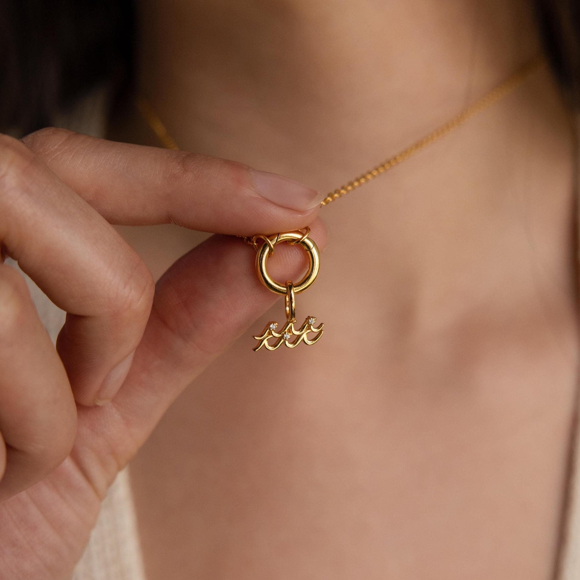 Gold necklace with a unique pendant held by a hand against a neutral background