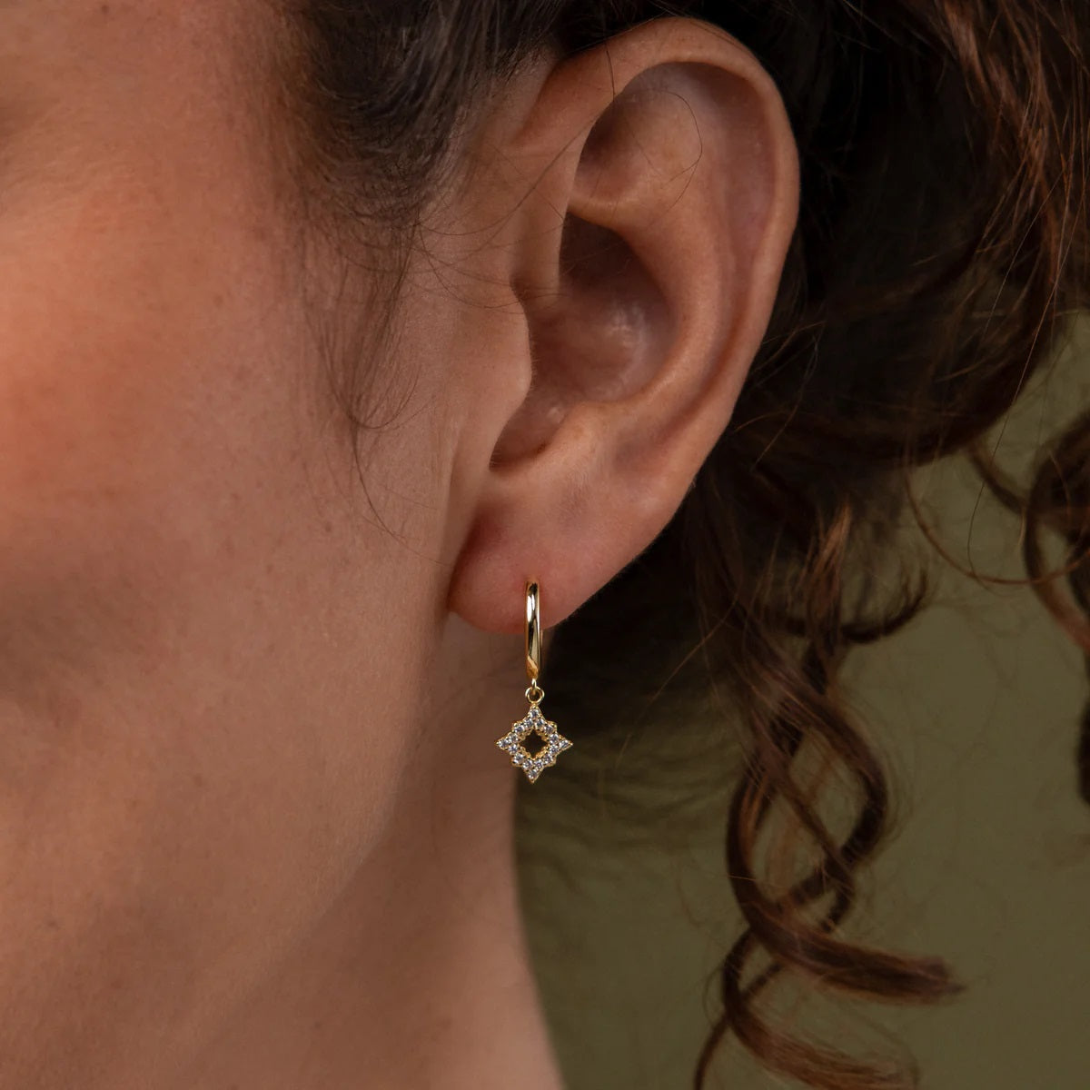 Close-up of an ear wearing a gold earring with a dark gemstone.